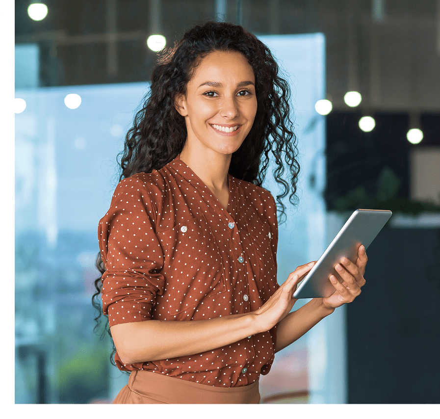 img A person in a brown polka dot shirt smiles while holding a tablet in an office setting.